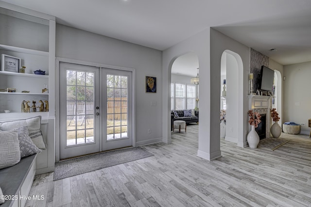 doorway with a large fireplace, baseboards, arched walkways, wood finished floors, and french doors