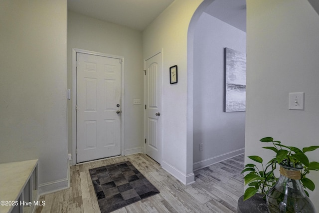 foyer entrance with arched walkways, baseboards, and light wood finished floors