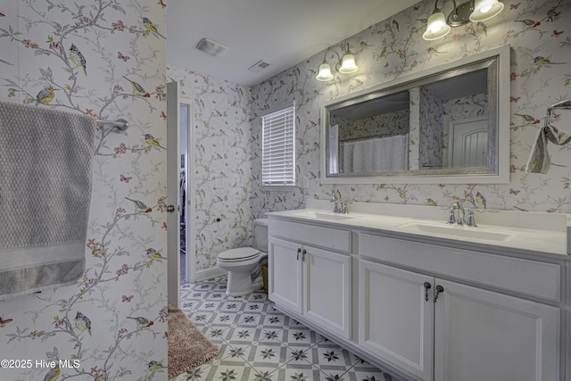 bathroom featuring double vanity, visible vents, toilet, a sink, and wallpapered walls