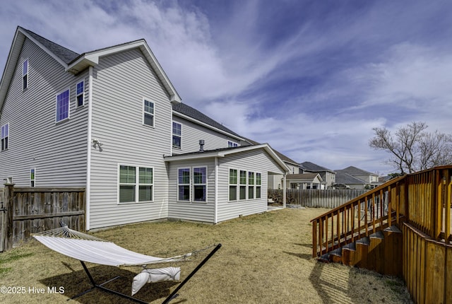 rear view of property featuring roof with shingles, a fenced backyard, and a lawn