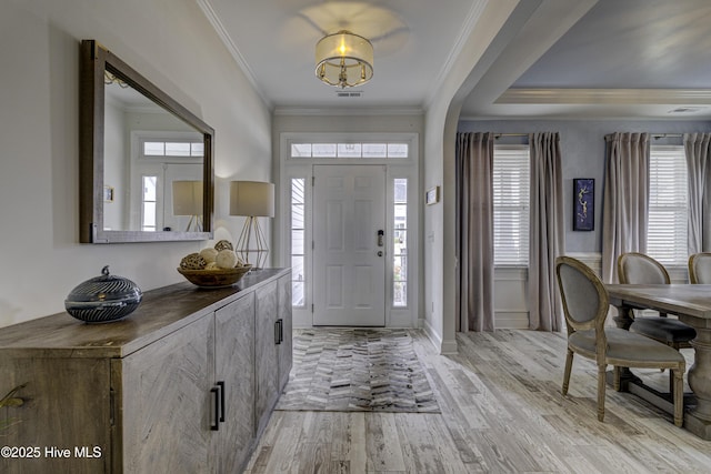 foyer with light wood finished floors, plenty of natural light, visible vents, and crown molding