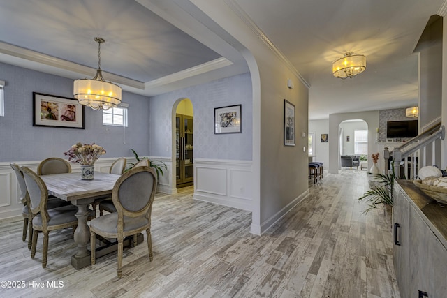 dining space featuring arched walkways, a wainscoted wall, a chandelier, and light wood-style floors