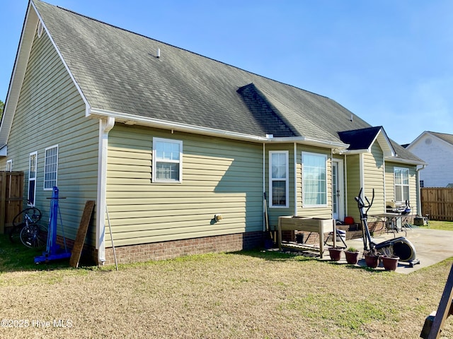 back of house featuring roof with shingles, a patio, a lawn, and fence