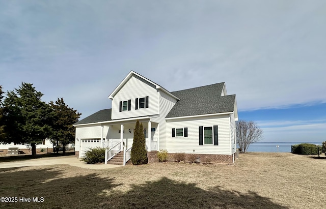 traditional-style home with a shingled roof, a front yard, concrete driveway, and covered porch