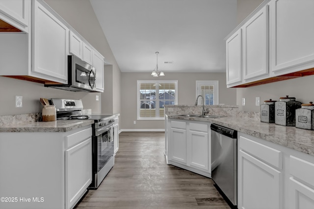 kitchen featuring appliances with stainless steel finishes, white cabinetry, a sink, wood finished floors, and a peninsula