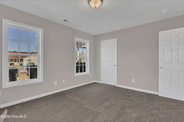 empty room with dark colored carpet, visible vents, and baseboards