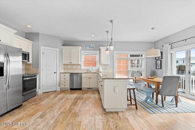 kitchen featuring light wood finished floors, decorative backsplash, appliances with stainless steel finishes, a peninsula, and a sink