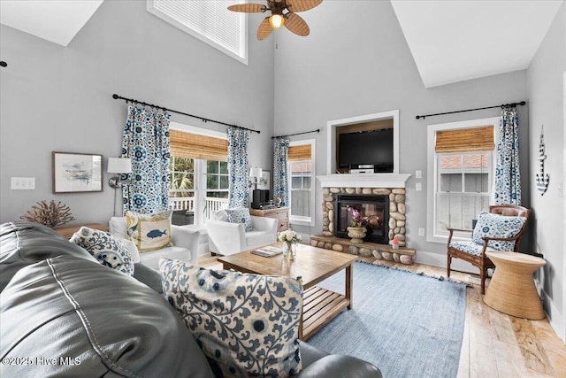 living room with ceiling fan, a fireplace, wood finished floors, a towering ceiling, and baseboards