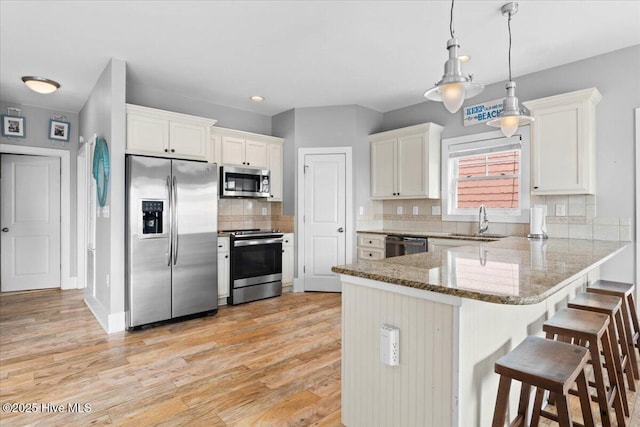 kitchen featuring a kitchen bar, a sink, tasteful backsplash, appliances with stainless steel finishes, and a peninsula