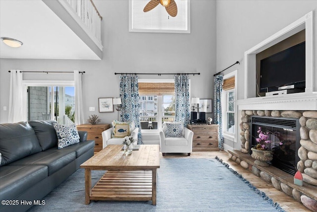 living room with a healthy amount of sunlight, a stone fireplace, a towering ceiling, and wood finished floors