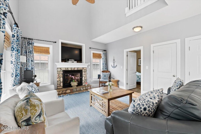 living area featuring wood finished floors, a high ceiling, a stone fireplace, baseboards, and ceiling fan