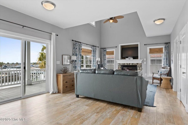 living area with high vaulted ceiling, a fireplace, a ceiling fan, and light wood finished floors
