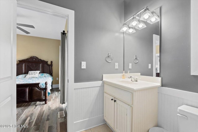 bathroom with a ceiling fan, a wainscoted wall, vanity, and toilet