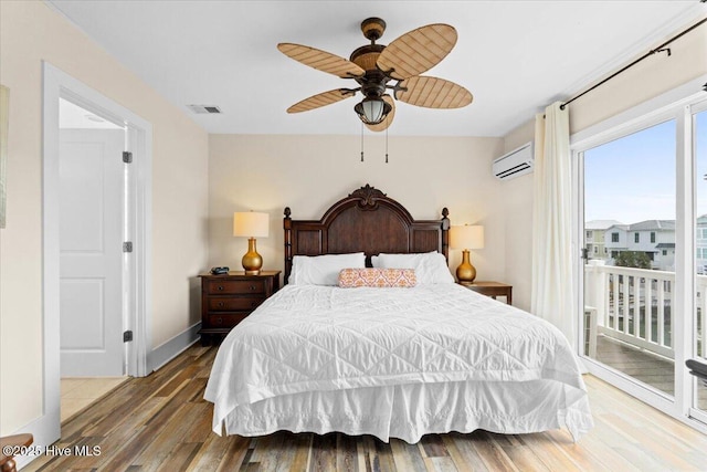bedroom with a wall mounted air conditioner, visible vents, wood finished floors, baseboards, and access to exterior