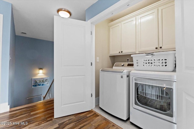 clothes washing area featuring visible vents, wood finished floors, washing machine and clothes dryer, and cabinet space