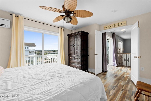 bedroom featuring a ceiling fan, wood finished floors, baseboards, a wall mounted AC, and access to exterior