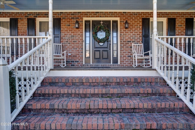 entrance to property featuring a porch and brick siding