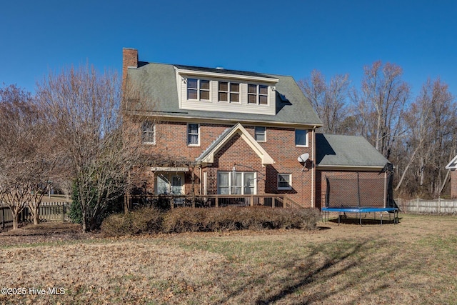 rear view of house featuring a lawn, a chimney, a trampoline, fence, and brick siding