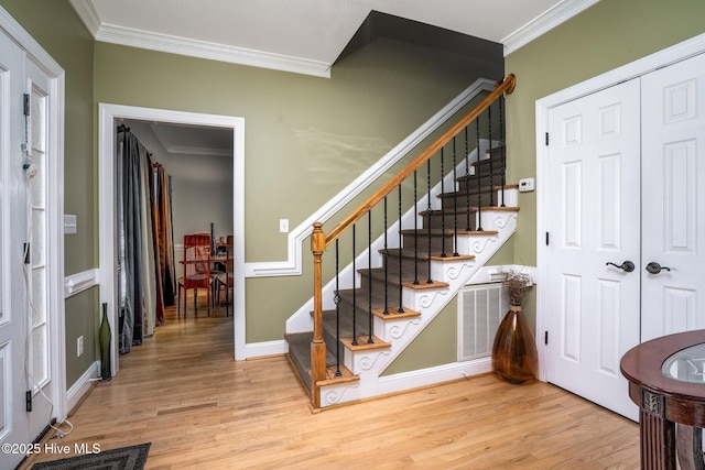 stairs with crown molding and wood finished floors