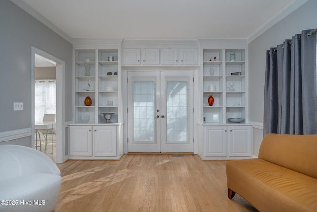 living area featuring light wood-type flooring, built in shelves, ornamental molding, and french doors