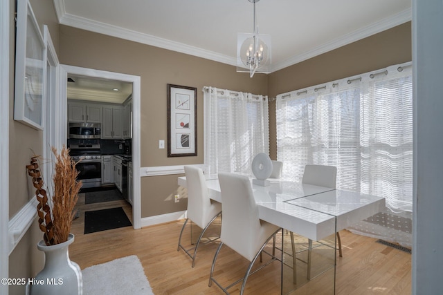 dining area with baseboards, visible vents, ornamental molding, light wood-style floors, and a chandelier