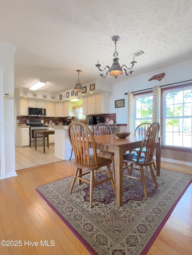 dining area featuring visible vents, baseboards, light wood-style floors, and a textured ceiling