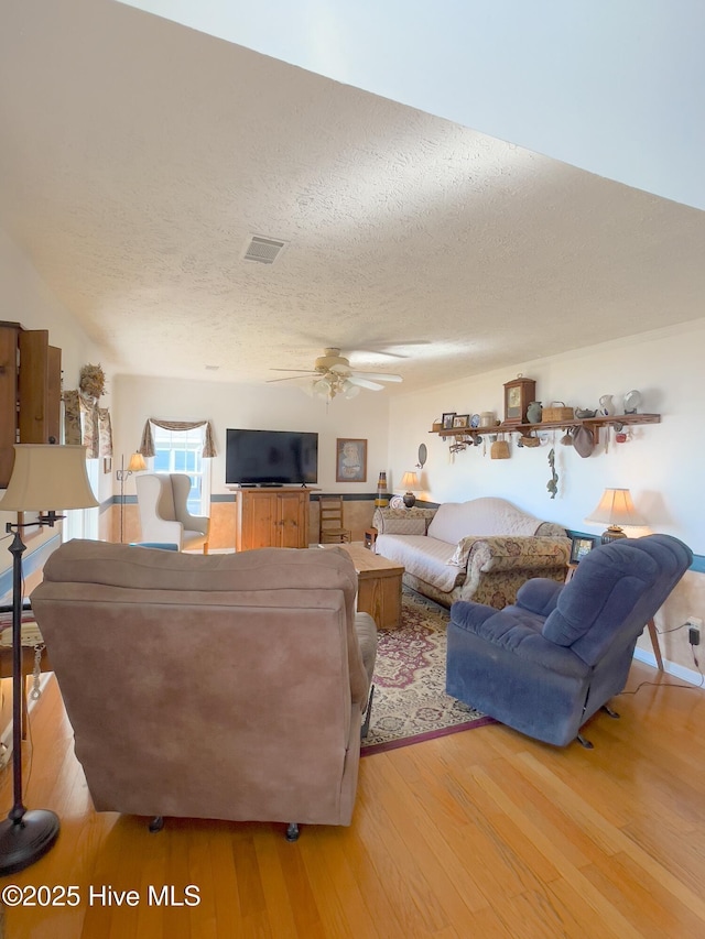 living area with visible vents, light wood-style flooring, a textured ceiling, and ceiling fan