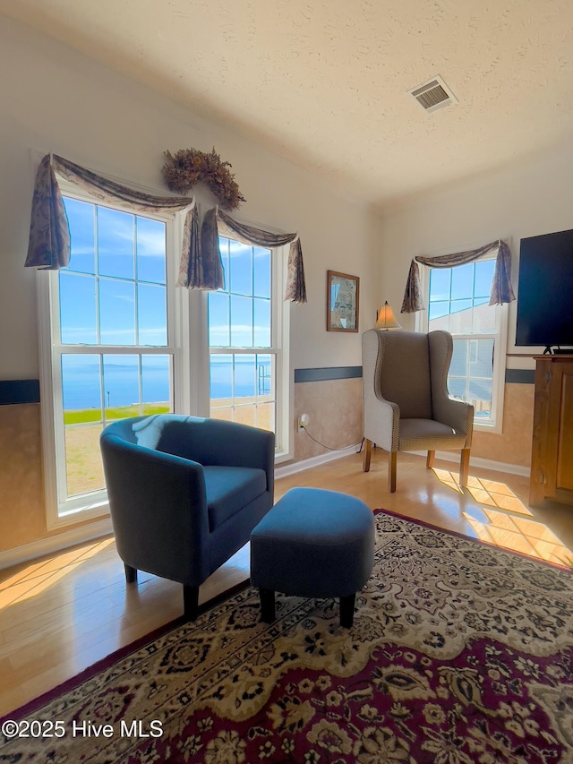 sitting room with visible vents, baseboards, a textured ceiling, and wood finished floors