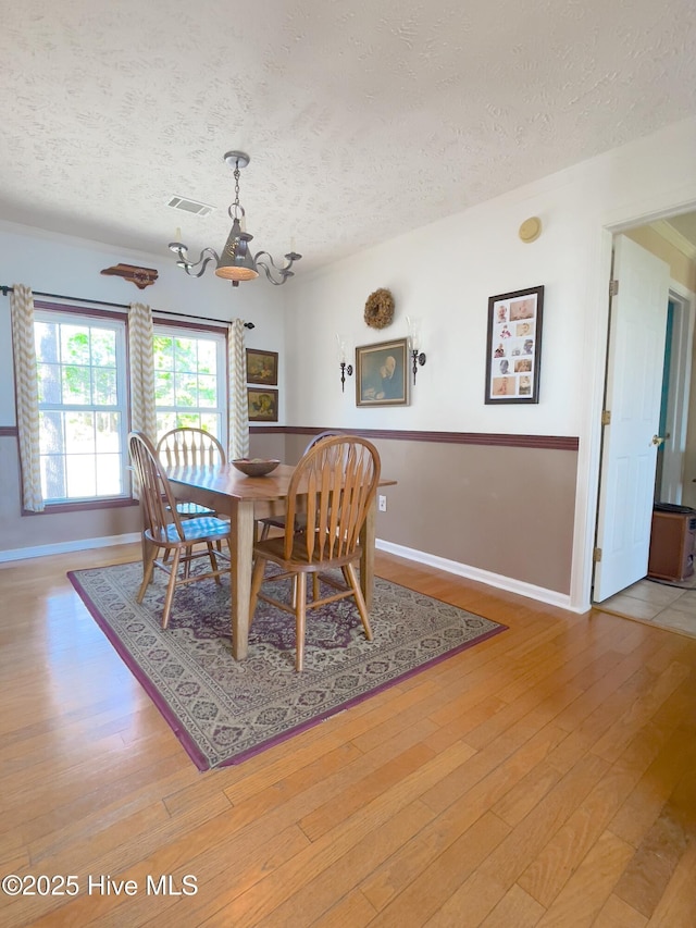 dining area featuring an inviting chandelier, light wood-style floors, visible vents, and a textured ceiling