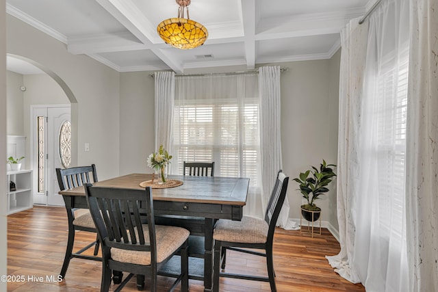 dining space featuring arched walkways, beamed ceiling, light wood-type flooring, and visible vents