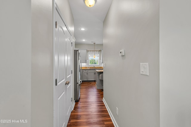 hall with dark wood-type flooring, recessed lighting, a sink, and baseboards