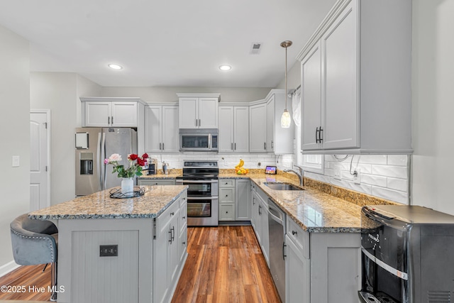 kitchen featuring stainless steel appliances, wood finished floors, a sink, backsplash, and a center island