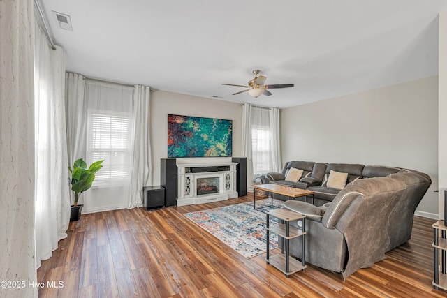 living area featuring ceiling fan, visible vents, a fireplace, and wood finished floors