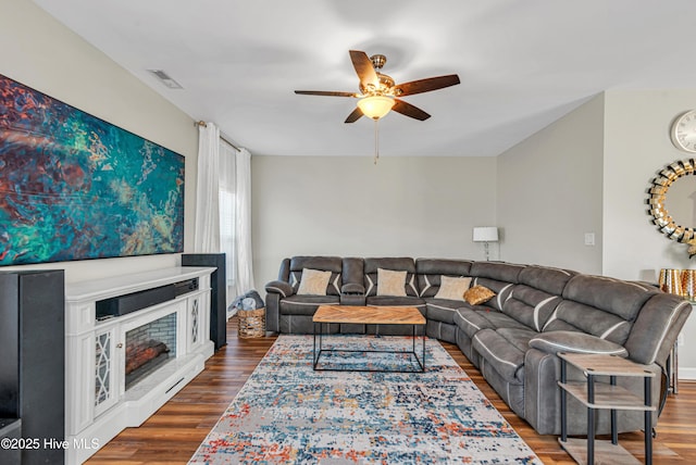 living room featuring dark wood-style floors, a fireplace, visible vents, and a ceiling fan