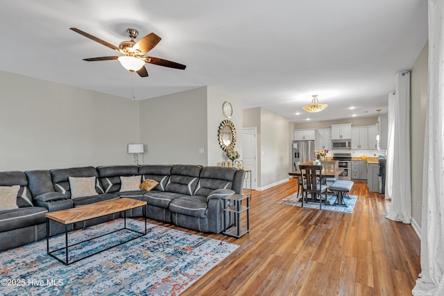 living area with a ceiling fan, light wood-style flooring, and baseboards