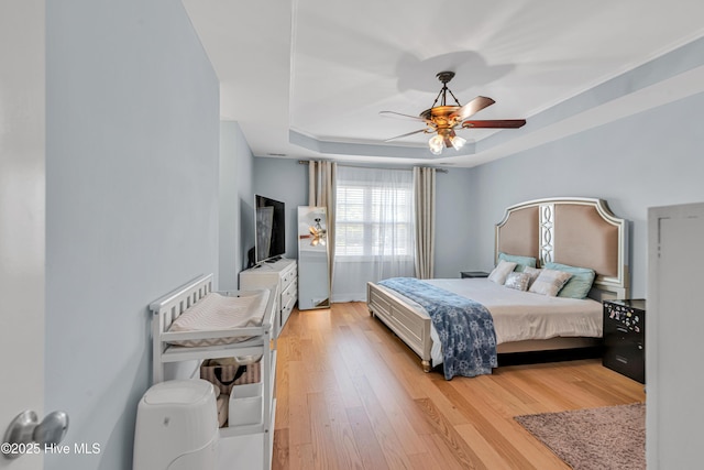 bedroom with ceiling fan, light wood finished floors, and a raised ceiling