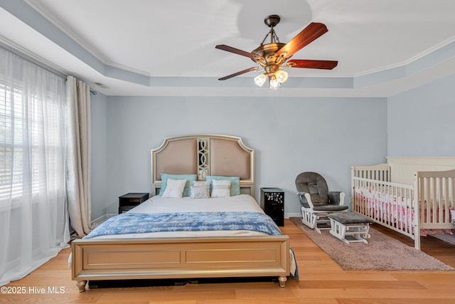 bedroom featuring ceiling fan, ornamental molding, a raised ceiling, and light wood-style floors