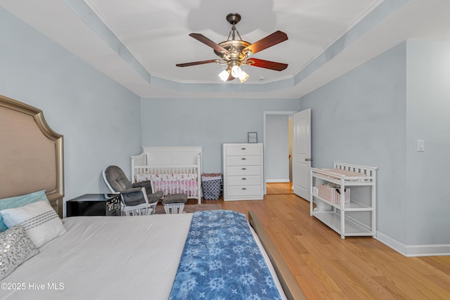 bedroom with baseboards, a raised ceiling, ceiling fan, ornamental molding, and wood finished floors