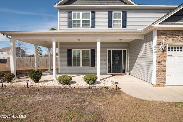 view of front of house featuring stone siding, fence, and covered porch