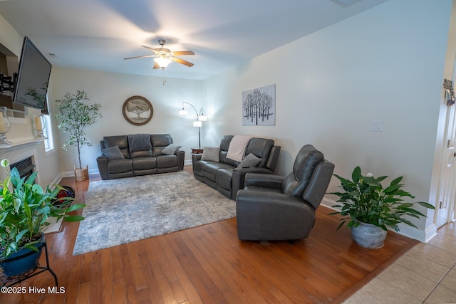 living room featuring baseboards, a ceiling fan, wood finished floors, and a glass covered fireplace