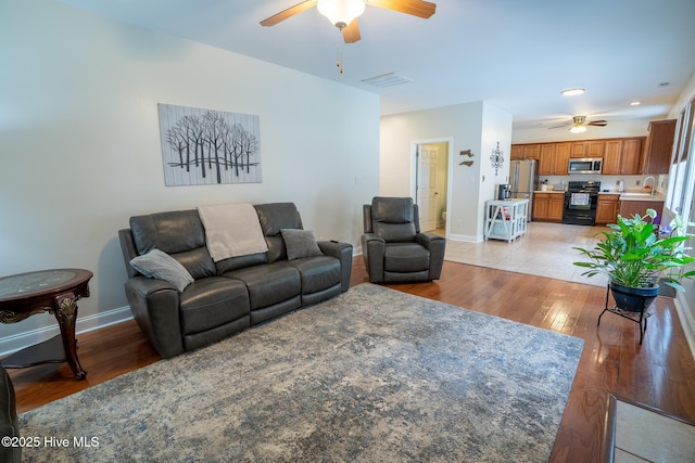 living room featuring light wood-style floors, visible vents, baseboards, and a ceiling fan