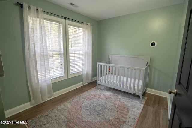 bedroom with a nursery area, wood finished floors, visible vents, and baseboards