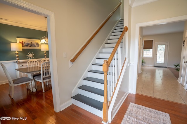 stairway with a notable chandelier, ornamental molding, wood finished floors, and baseboards