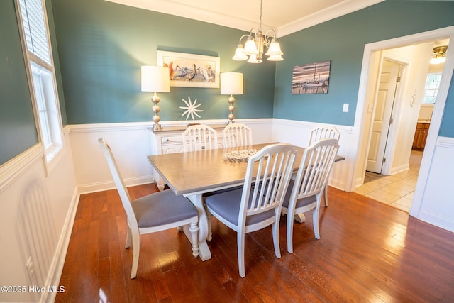 dining space featuring ornamental molding, a wainscoted wall, a notable chandelier, and hardwood / wood-style flooring