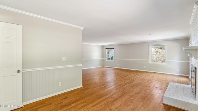 unfurnished living room with light wood-style floors, a fireplace, crown molding, and a wainscoted wall