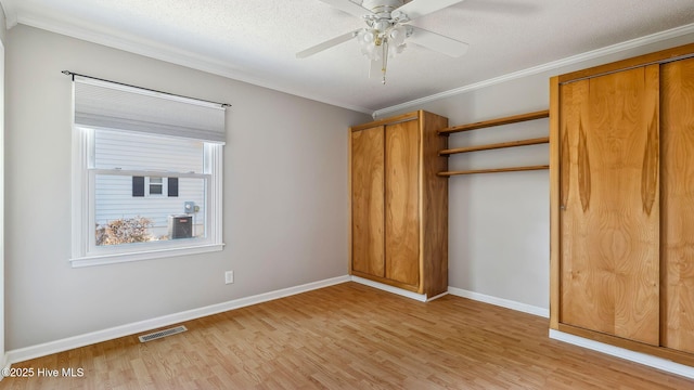 unfurnished bedroom with visible vents, baseboards, light wood-style flooring, ornamental molding, and two closets