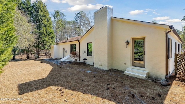 back of property with entry steps, brick siding, and a chimney