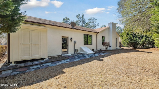 back of house with a chimney and stucco siding