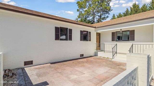 property entrance with crawl space, a shingled roof, a patio, and brick siding