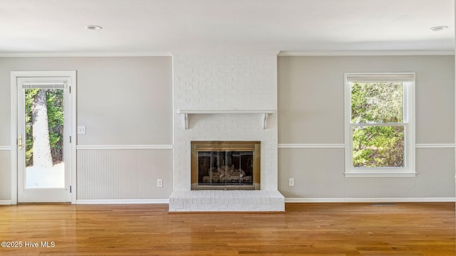 unfurnished living room with a wainscoted wall, ornamental molding, wood finished floors, and a healthy amount of sunlight